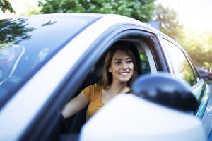 Jeune femme contente dans sa voiture, car elle a fait des économies en choisissant bien, entre l'abattement de 10% et les indemnités kilométriques.